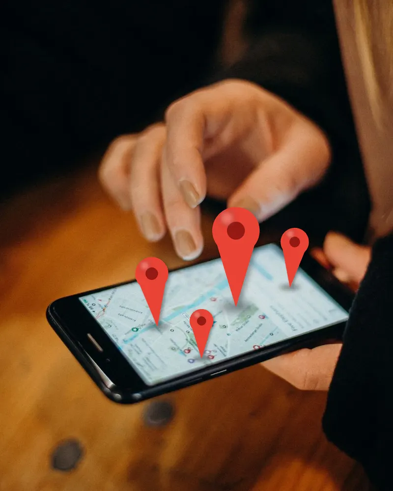 Google Maps SEO services: a hand tapping a map on a phone with red location pins rising from the screen